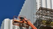 A red cherry picker sits in front of a patterned steel wall.